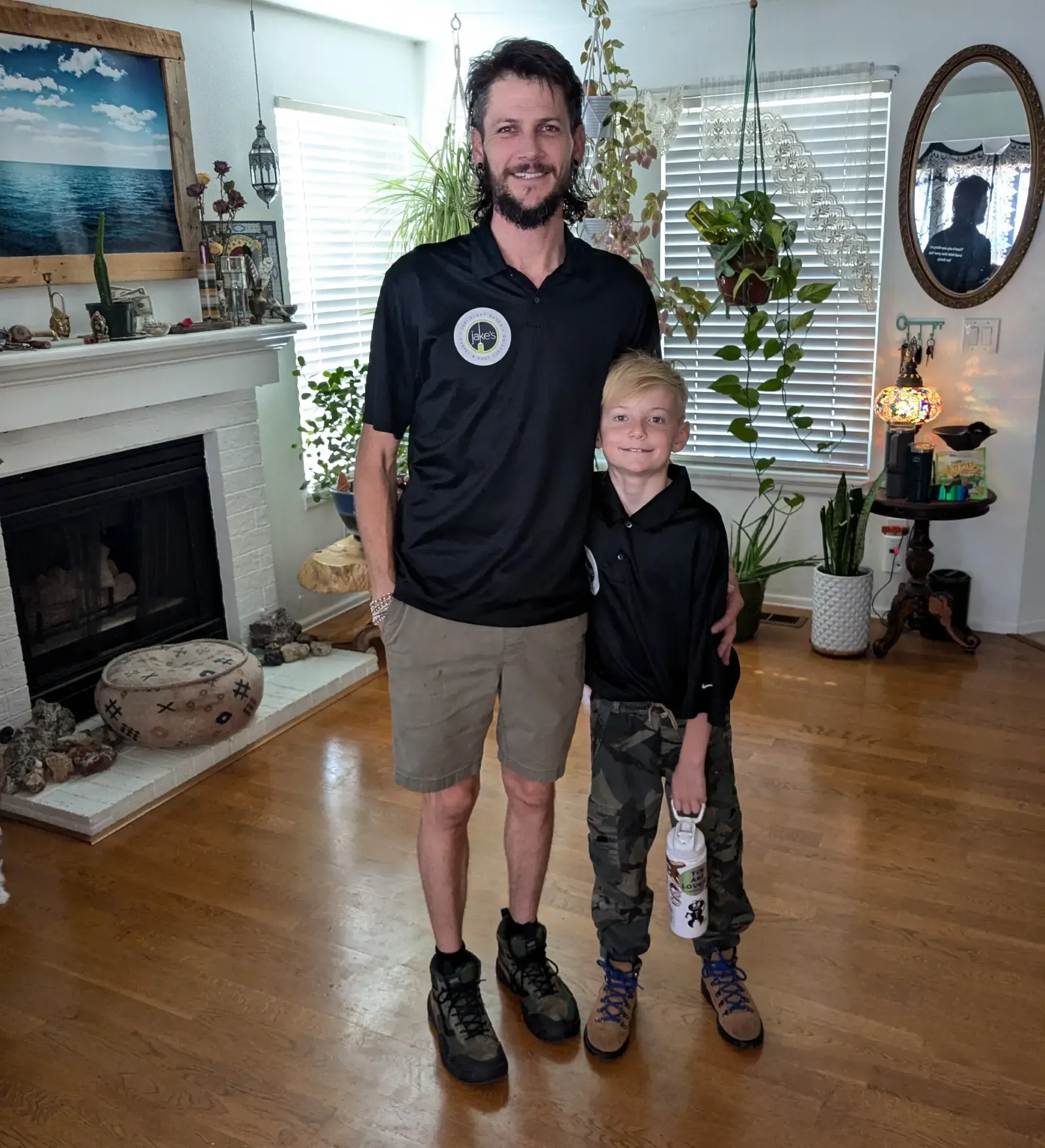 Jake and his son standing in a bright living room by the fireplace, both in Jake's black work shirts